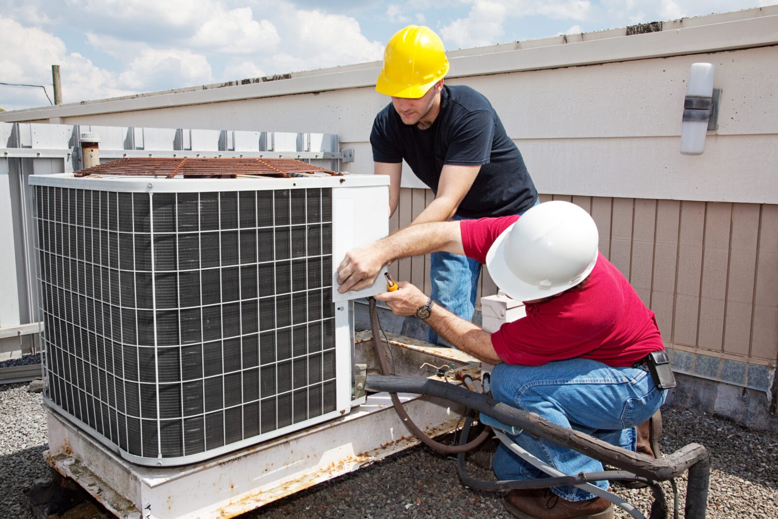 Two workers repairing an air conditioning unit on a rooftop.