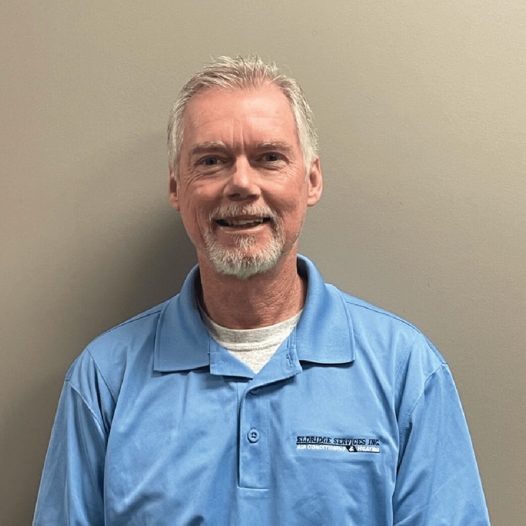 Man in a light blue polo shirt smiling against a gray background.