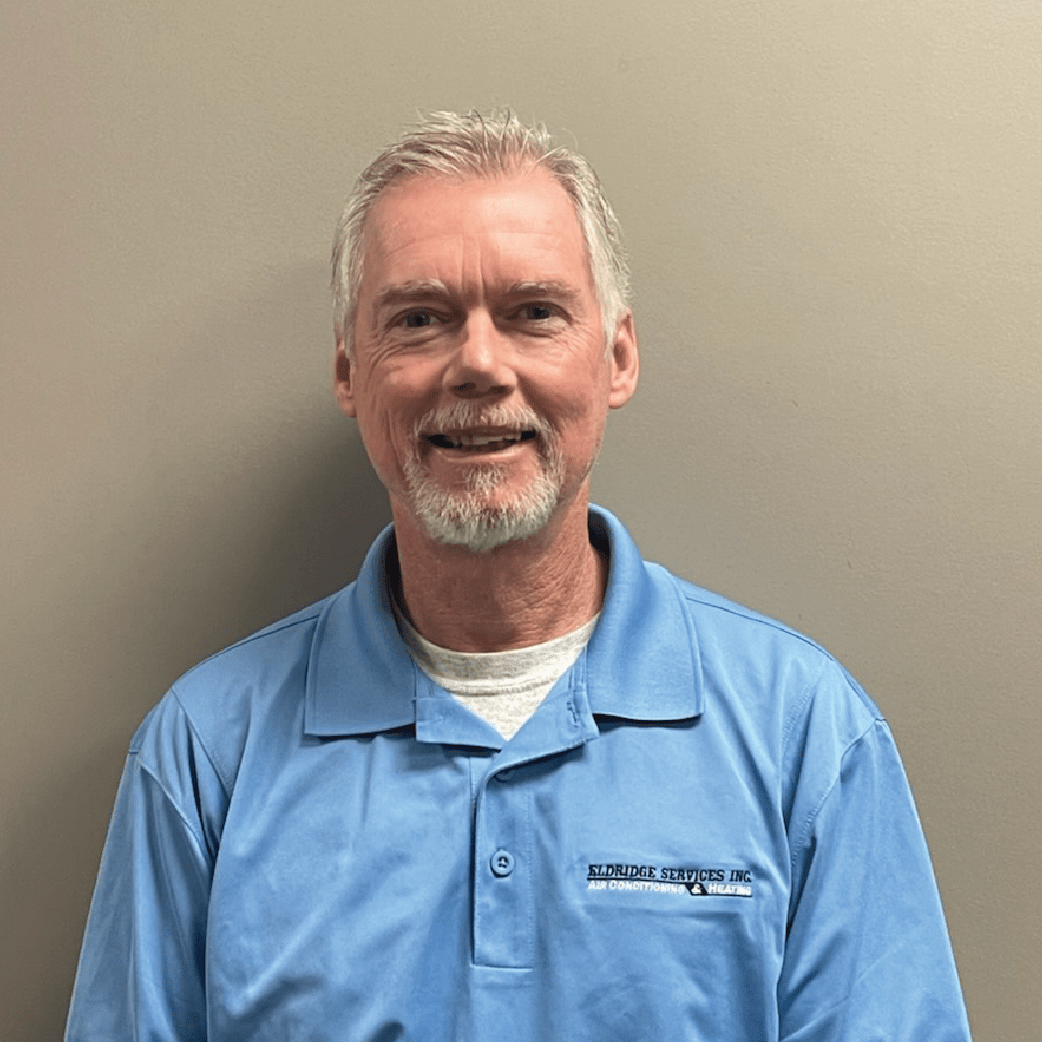 Man in a light blue polo shirt smiling against a gray background.